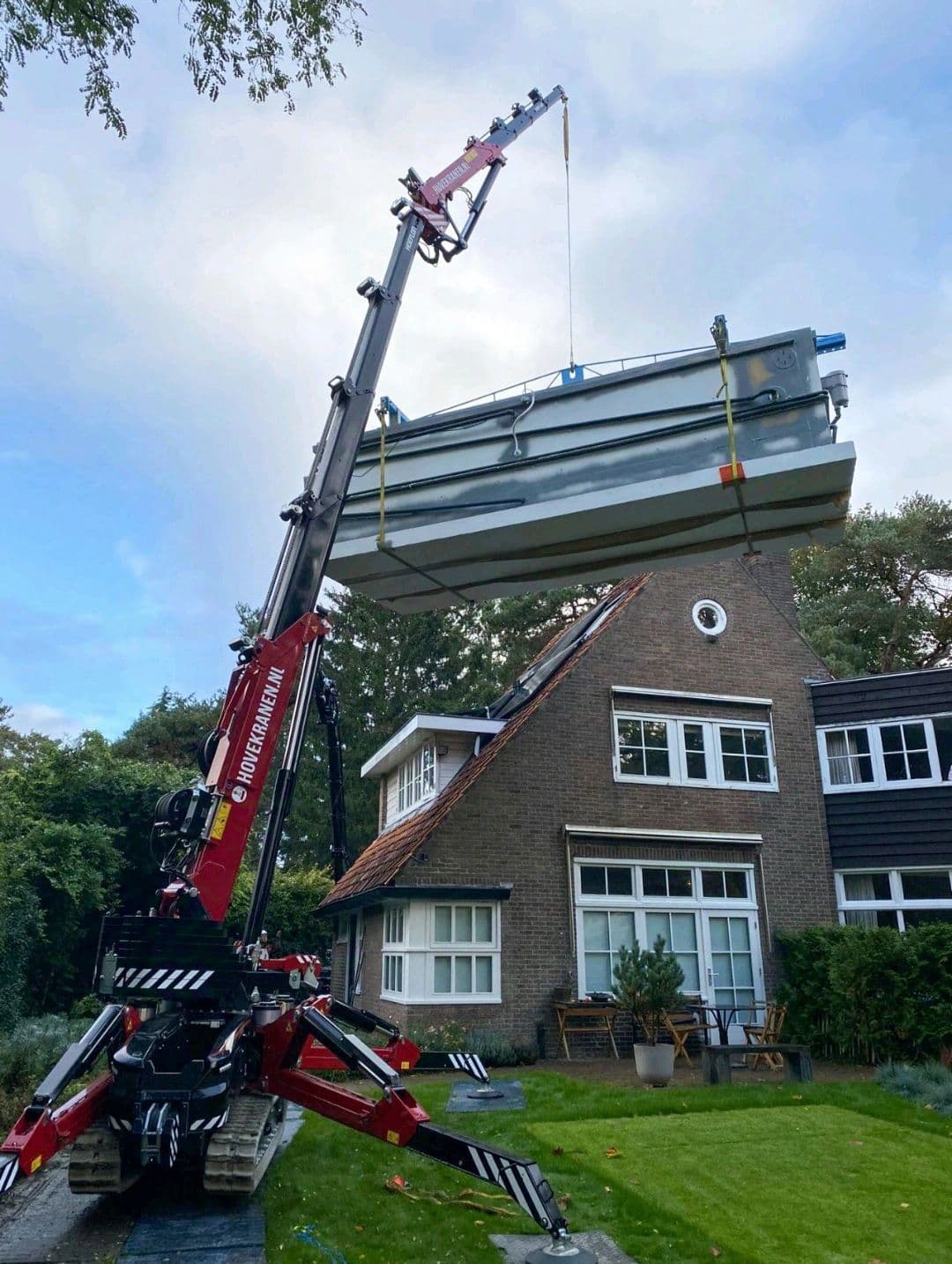 Mini-grue Hoeflon soulevant un objet lourd devant une maison.