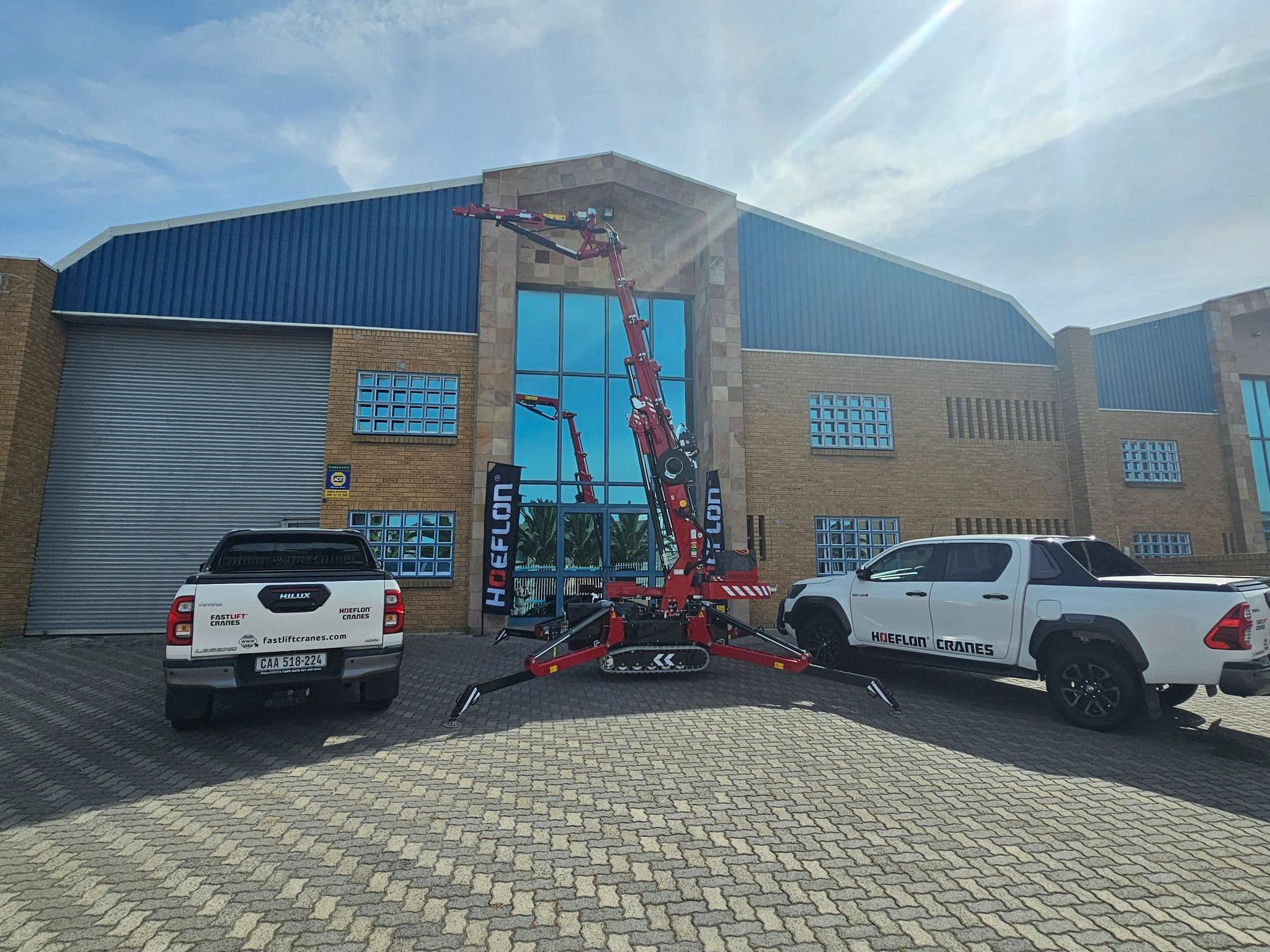Grue Hoeflon devant un bâtiment avec deux véhicules de Fastlift Cranes.