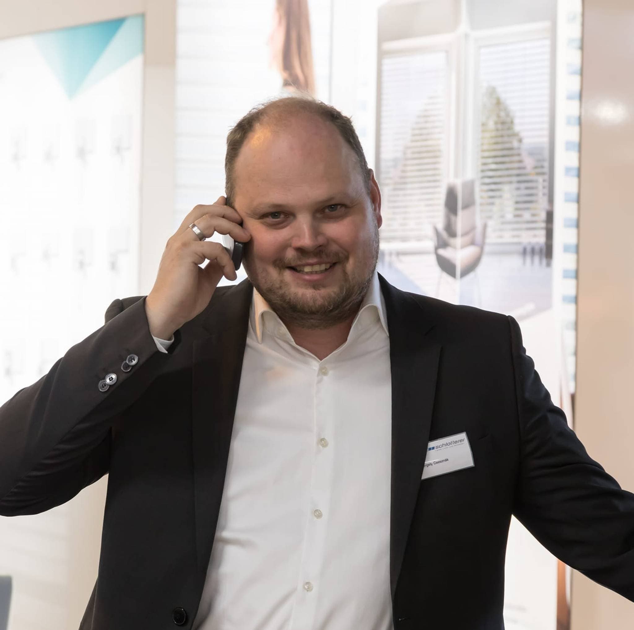 Gergely Metromont, homme en costume, parlant au téléphone lors d'une exposition.