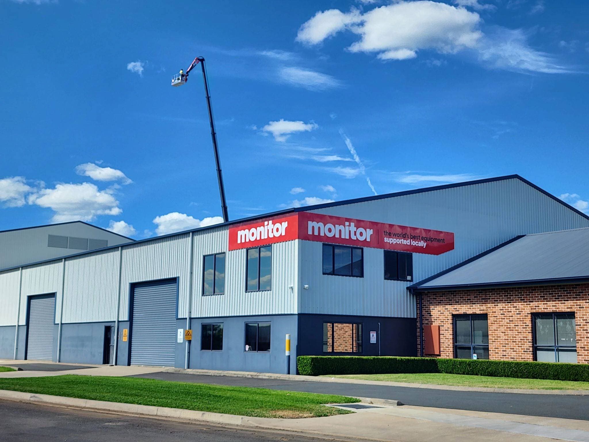 Nacelle élévatrice devant un bâtiment avec un panneau monitor à côté.