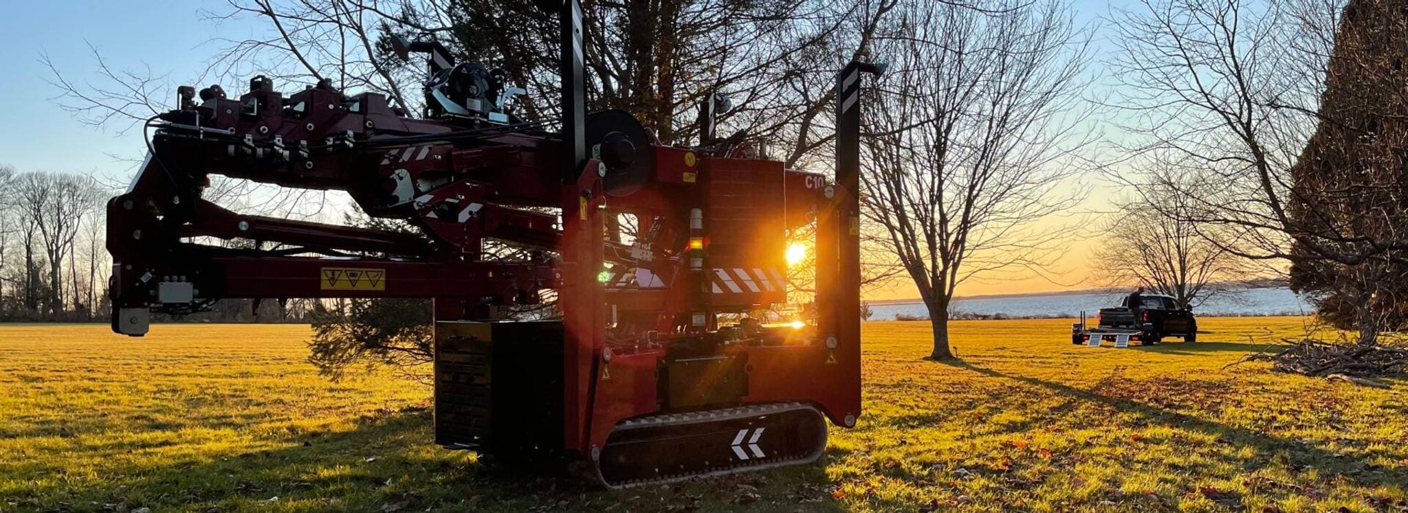 Grue Hoeflon au soleil, avec un camion en arrière-plan et des arbres autour.